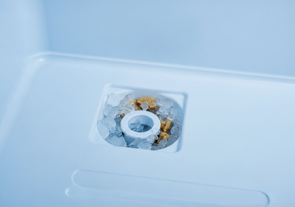 Clogged refrigerator defrost drain hole with ice buildup and food debris blocking the freezer floor drain opening