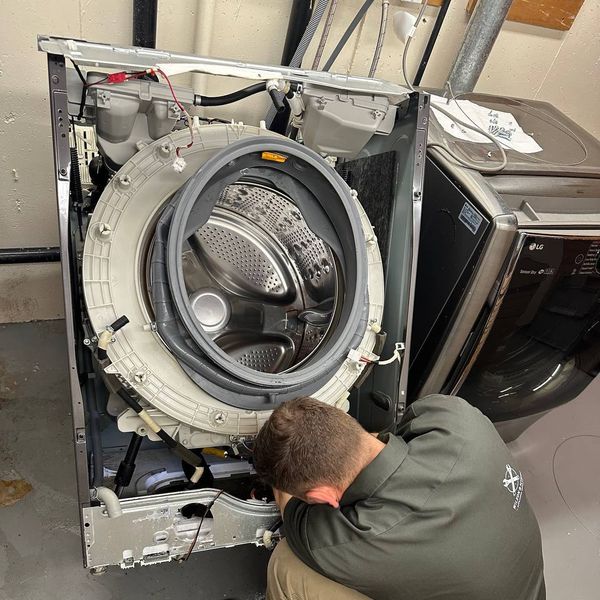 Front-load washer door opening showing boot seal inspection: bottom fold pulled forward, flashlight inspection area highlighted, tear-prone zone at bottom of pleat indicated