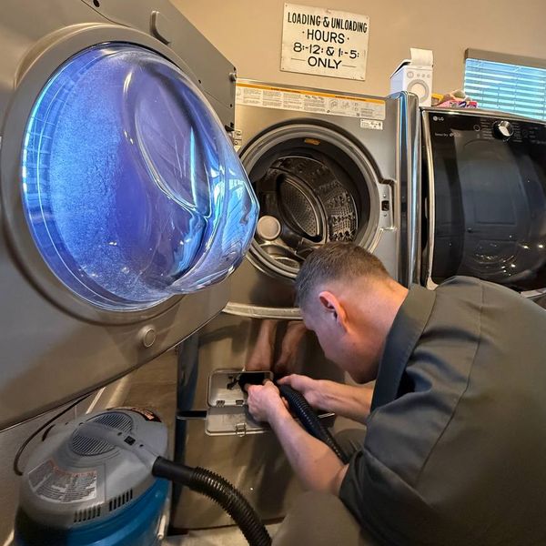 Diagram showing drain pump location on front-load washer: pump filter access door lower-front, pump body behind access panel, drain hose outlet at rear lower corner