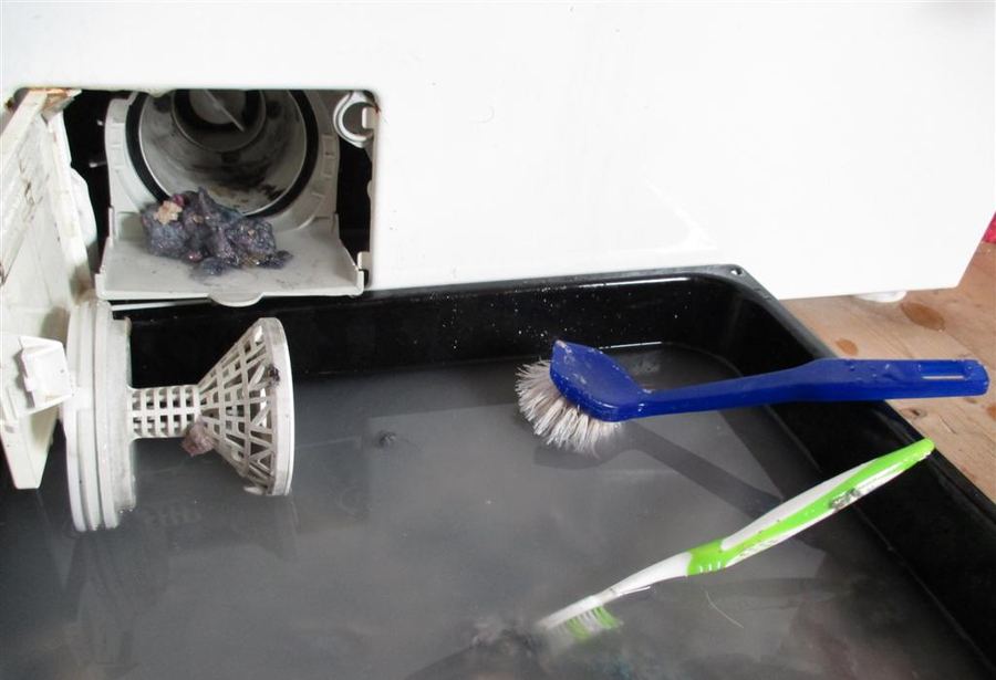 Front-load washing machine drain pump filter removed, showing clog debris inside housing; washer not draining cause #1
