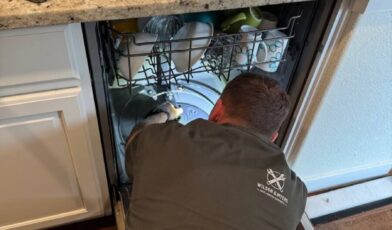 Wilson and Myers technician inspecting the filter and drain pump area inside an open Bosch dishwasher during an E24 drain fault repair in a Denver Metro kitchen
