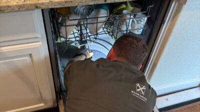 Wilson and Myers technician inspecting the filter and drain pump area inside an open Bosch dishwasher during an E24 drain fault repair in a Denver Metro kitchen