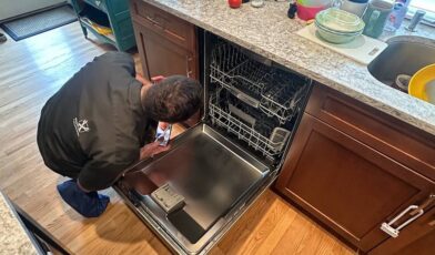 Wilson and Myers technician kneeling at an open dishwasher in a Denver kitchen to reach the filter in the tub floor.
