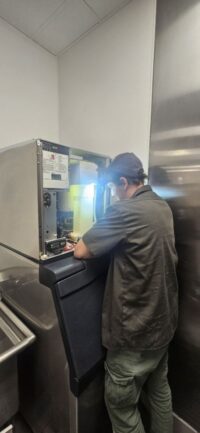 Technician checking an ice machine control panel with a work light