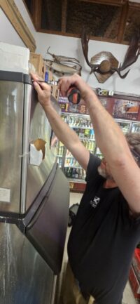 Technician working on an undercounter ice machine behind a bar