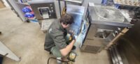 Technician working on stainless prep refrigeration in a commercial kitchen