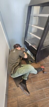 Technician servicing a glass door cooler during a temperature call