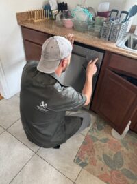 Technician checking the dishwasher drain connection under the sink in Denver Metro