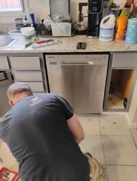 Technician working at the base of a dishwasher on the drain line