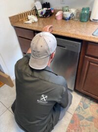 Technician reaching under the counter to check a dishwasher drain hose