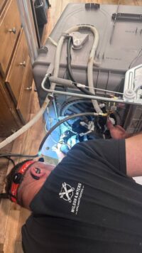 Technician tracing dishwasher hoses with a headlamp
