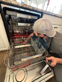 Technician removing the lower rack to reach the dishwasher spray arm
