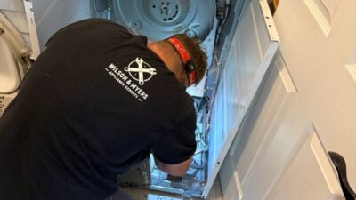 Wilson and Myers technician working inside a white top-load dryer during a no-heat repair in a Denver Metro home