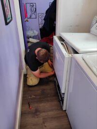 Technician checking the space behind a washer and dryer pair