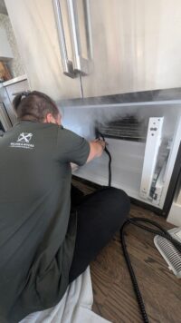 Technician reaching behind the freezer panel to check the evaporator