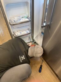 Technician kneeling at the base of a freezer