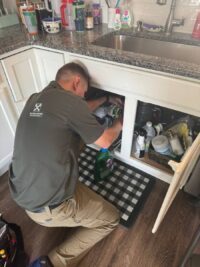 Technician servicing a garbage disposal under a kitchen sink in Denver Metro
