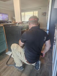 Technician checking the gas connection behind a range