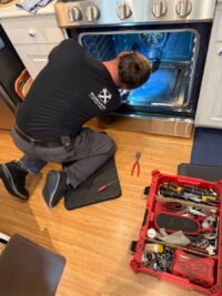 Technician kneeling at an open oven during a luxury range repair
