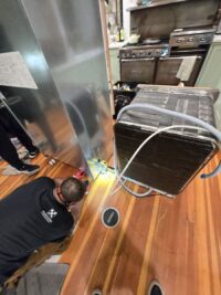 Condenser grille removed for cleaning during refrigerator maintenance