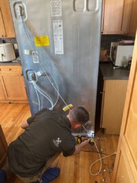 Technician connecting refrigerant recovery lines during refrigerator sealed system service in Denver Metro