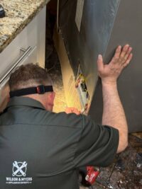 Technician working at the exposed back of a refrigerator during sealed system diagnosis