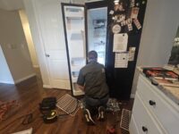 Technician working behind a refrigerator to trace a noise complaint