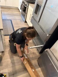 Technician checking the compressor area at the base of a refrigerator