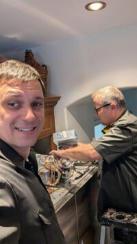 Two technicians reviewing a refrigerator control board with the homeowner