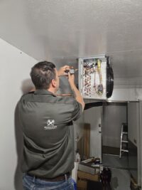Technician on a ladder servicing a walk-in evaporator