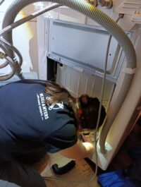 Technician reaching under a washer to check the drain pump