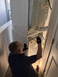Technician working behind a front load washer in a tight laundry space