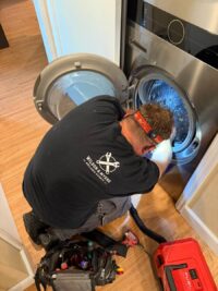 Technician working inside a top load washer tub with tools at hand