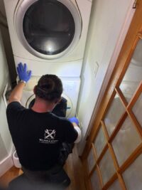 Technician in gloves examining a front load washer drum