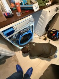 Technician on the floor servicing the lower assembly of a front load washer