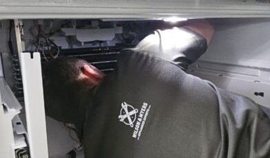 Wilson and Myers technician working inside an opened refrigerator compartment on a Denver Metro service call