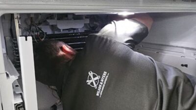 Wilson and Myers technician working inside an opened refrigerator compartment on a Denver Metro service call